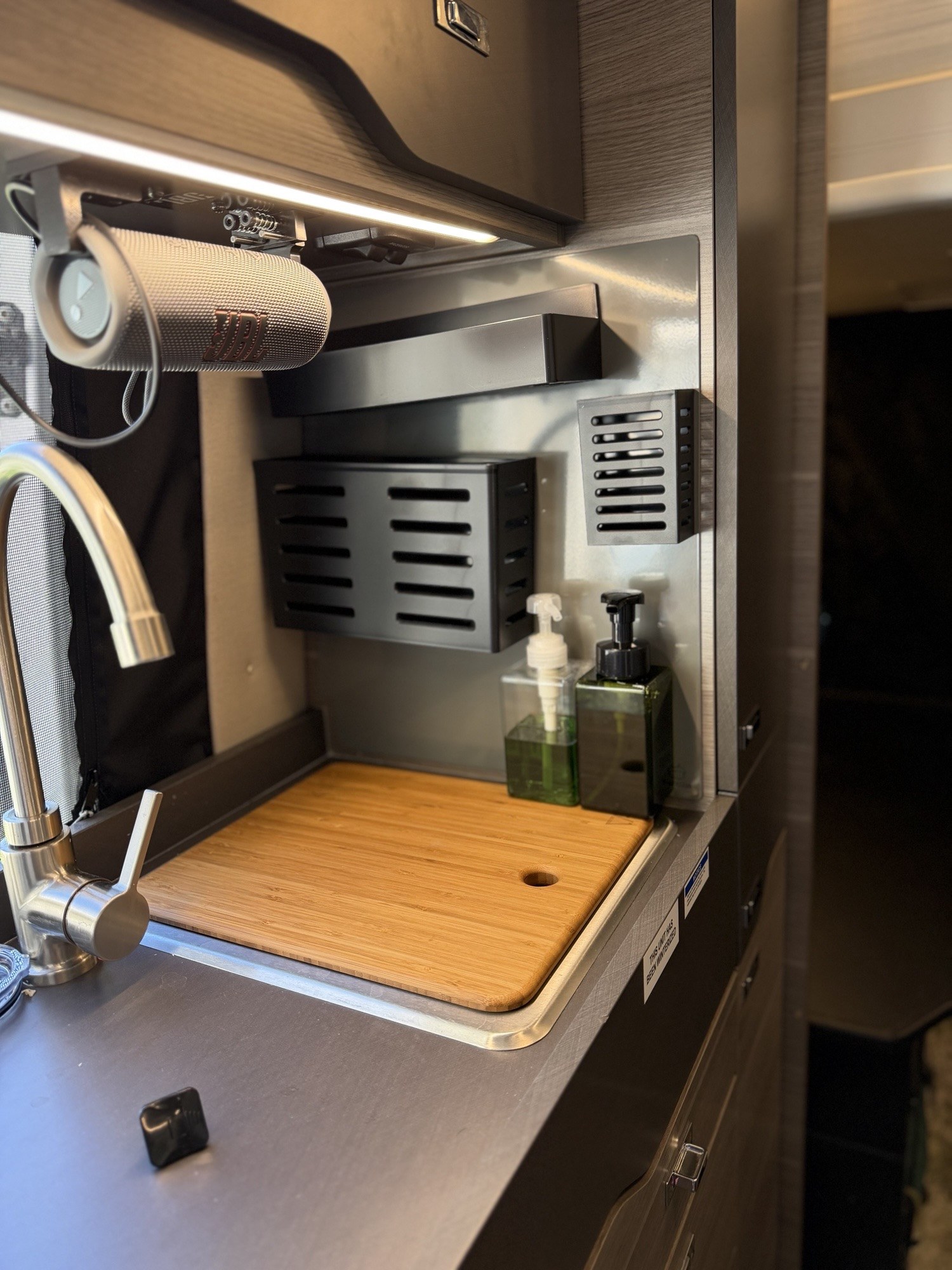Customer photo from Frederick T of a Slate Acorn Stash Kitchen Magnetic Board behind the sink in a Jayco Terrain 19Y, with a bamboo sink cover, a wide magnetic shelf on top, a wide slotted basket on the left, and a tall basket on the right.